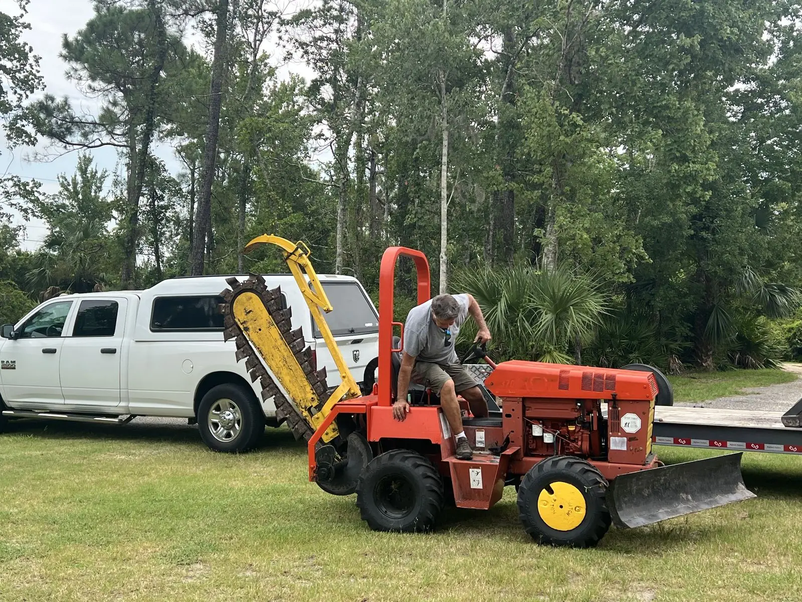 Operator riding a chain trencher cutting a straight utility trench across sandy ground on a Central Florida property