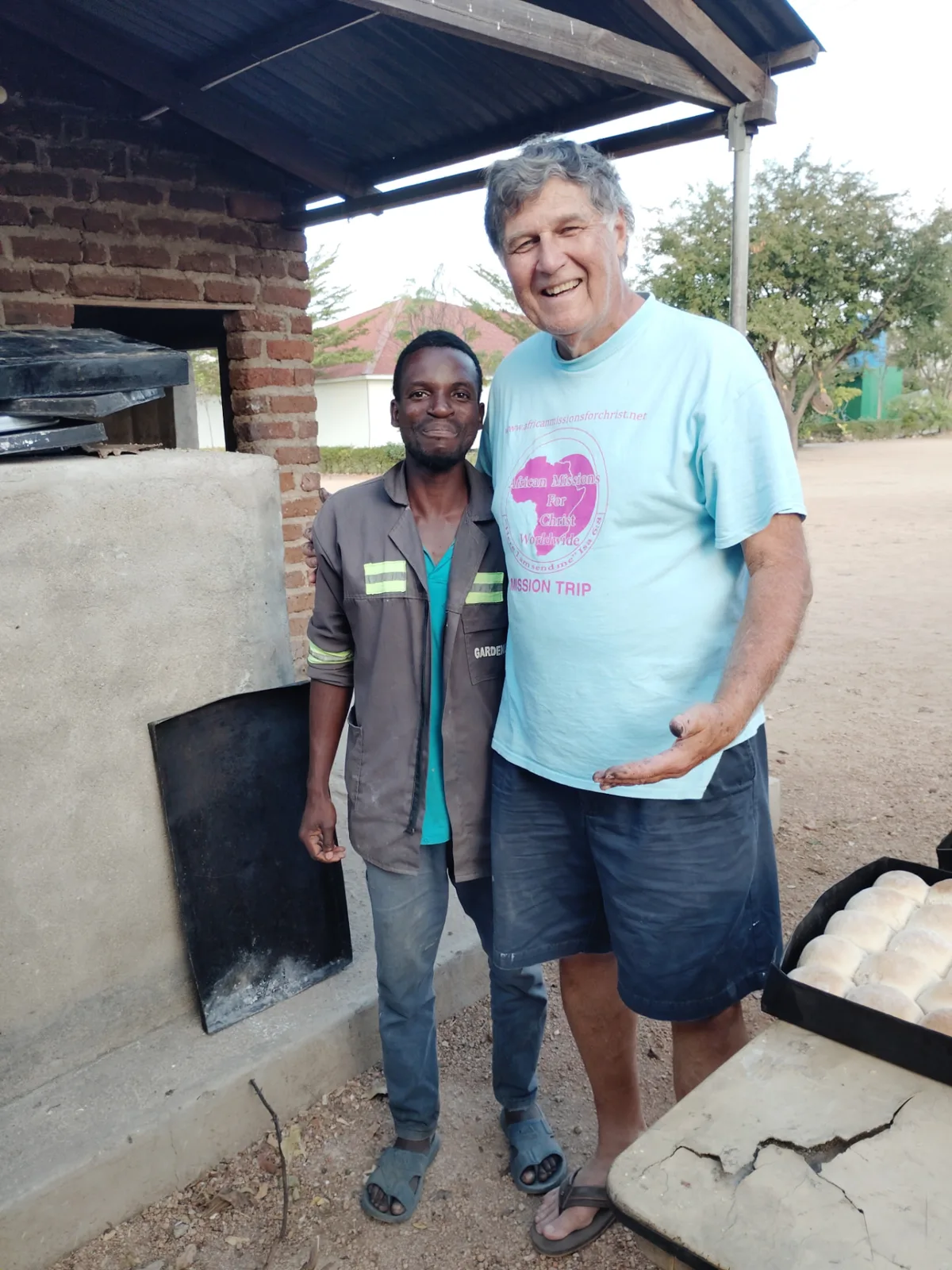 Landon Thomas standing with a local worker beside a brick bread oven at the African Missions For Christ Worldwide site
